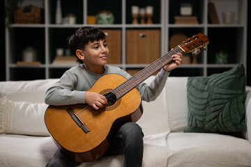 Obraz premium Young boy learning playing acoustic guitar at home