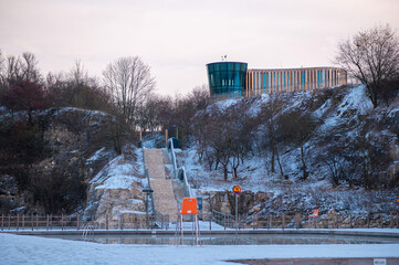 Snow-covered outdoor swimming pool with a modern building on a hill.