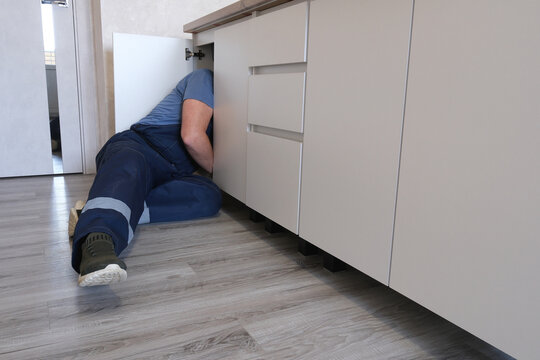 Plumber working fixing leak under kitchen sink cabinet