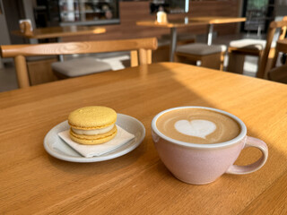 Cup of coffee with macaron pastry on wooden table in cafeteria close up