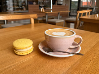 Cup of coffee with macaron pastry on wooden table in cafeteria close up