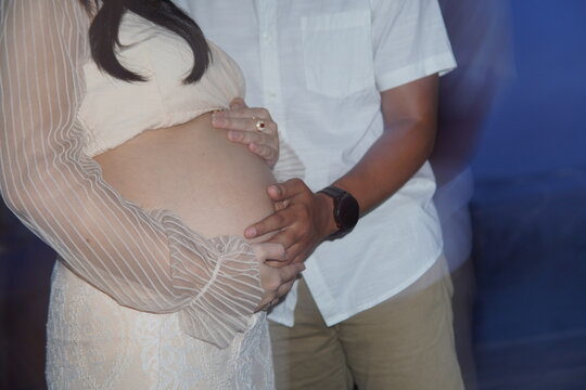Close-up of a pregnant woman’s bare belly gently cradled by her and her partner’s hands, photographed in soft evening light with blurry effect. - Powered by Adobe