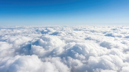 Aerial view of a sea of fluffy white clouds meeting a clear blue sky on a bright sunny day above earth