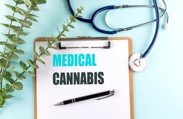 Text medical cannabis written on clipboard with stethoscope, pen, and green leaves on blue background 