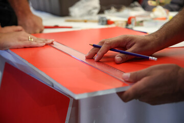 Skilled hands meticulously measure on a vibrant red surface, showcasing precision and craftsmanship in advertising, construction, or creative industrial projects.
