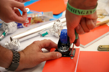 Hands skillfully attaching a blue caster wheel to a vibrant red board using a screwdriver. Innovative workshop project, showcasing creative design and hands-on assembly.
