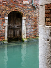 An old Venetian brick water door with turquoise reflections in the canal.