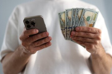 Online sevices or shopping concept. Man holds dollar bills and smartphone close-up