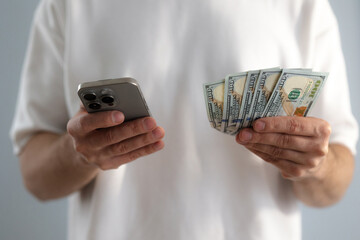 Online sevices or shopping concept. Man holds dollar bills and smartphone