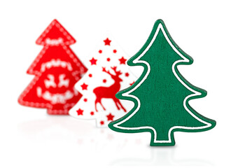Three Christmas trees on a white background, featuring a green wooden tree in the foreground and two softly blurred festive trees with red and white ornaments in the background.