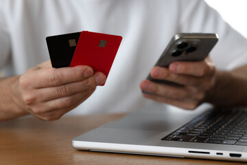 Man holds smartphone and credit cards next to laptop