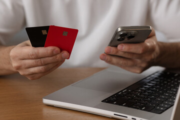 Online sevices concept. Man holds smartphone and credit cards next to laptop close-up