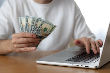 Online sevices or shopping concept. Man holds dollar bills next to laptop
