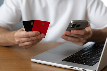 Online sevices. Man holds smartphone and credit cards next to laptop close-up