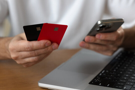 Online sevices. Man holds smartphone and credit cards next to laptop