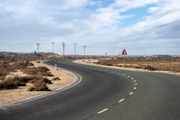 Dukhan, Qatar - November 25, 2025: A deserted asphalt road curving through a dry desert landscape. Road signs warn of an upcoming bend