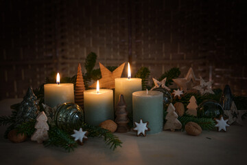 Three candles are lit for third Advent, fir branch, cinnamon star cookies and natural Christmas decoration from glass and wood, dark rustic background, copy space, selected focus