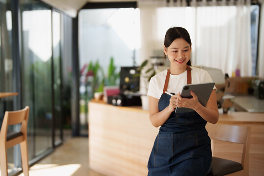 Asian woman barista managing coffee shop finances with tablet