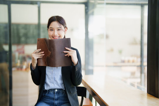Asian businesswoman smiling holding leather notebook in office
