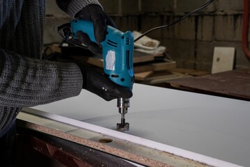 osoba w rękawicach ochronnych wierci otwór wiertarką w płycie wiórowej