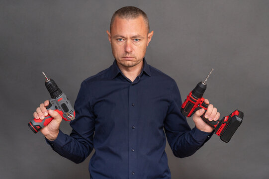 man holds two cordless screwdrivers, demonstrating the tools' ergonomic design and functionality. modern power tools ready for various DIY projects or professional tasks. on grey background