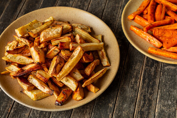 Two plates with root vegetables baked with honey and thyme: parsnip and carrot. Rustic wooden background.