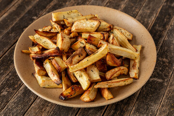 Parsnip roots baked with honey and thyme on a platter. Rustic wooden background.
