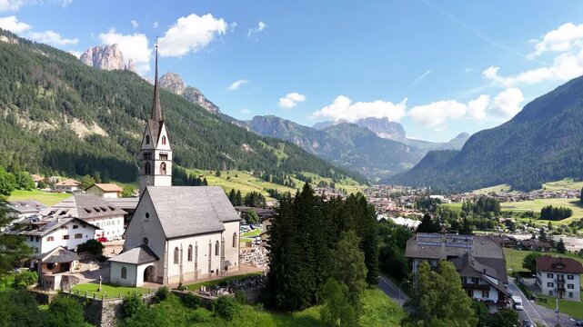 15 july 2024, Vigo di Fassa, Italy. Forward drone flight, aerial towards church and  centre of Vigo di Fassa in Val di Fassa village, beautiful Italian Dolomites during sunny summer day. Catholic chur