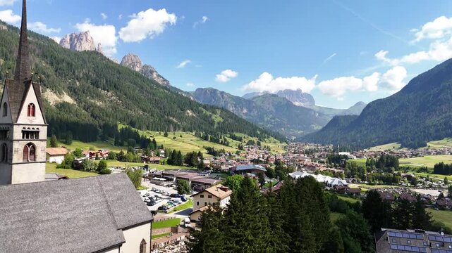 15 july 2024, Vigo di Fassa, Italy. Forward drone flight, aerial towards church and  centre of Vigo di Fassa in Val di Fassa village, beautiful Italian Dolomites during sunny summer day. Catholic chur