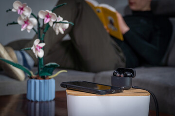 Smartphone and headphones set aside in the foreground while a man reads a book in the background. Concept of digital detox, disconnecting from technology, and returning to analog leisure