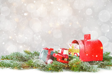 Snow-covered red mailbox with gift boxes and fir branches on bokeh background.