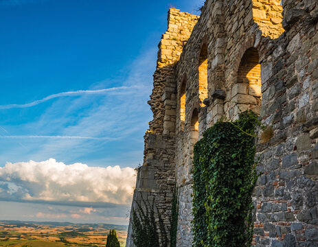 Ancient stone wall with arched windows overlooks Tuscan landscape. Sunlit. Perfect for travel blogs, history websites, or illustrating resilience and enduring beauty.