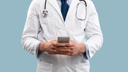 A healthcare professional stands wearing a white coat and a stethoscope. They are using a smartphone, possibly reviewing patient information in a modern clinical environment.