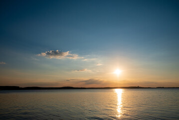 Vibrant colors fill the sky as the sun sets over a serene lake, creating a tranquil atmosphere