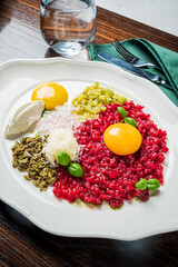 A vibrant dish featuring beef tartare topped with egg yolks and fresh herbs, served elegantly