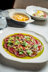 Savoring a beautifully plated beef carpaccio topped with herbs, vegetables, and vibrant sauces