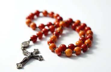 Strand of rosary beads with crucifix pendant rests on clean white background. Amber and red beads are separated by small metal spacers. This religious artifact is symbol of faith and prayer for many.