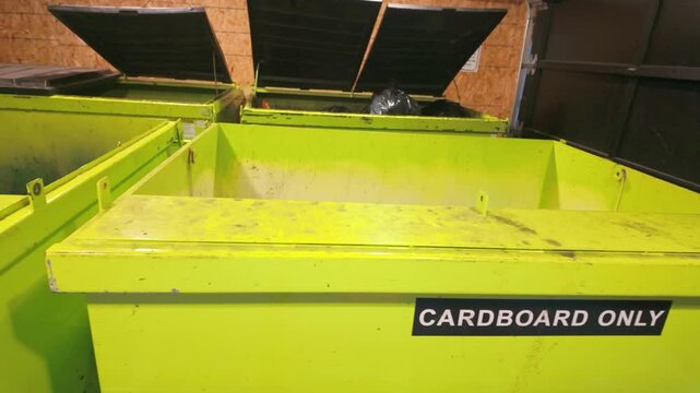 Set of bright green recycling bins marked for cardboard, situated in a wooden enclosure. The open lids suggest active use, emphasizing sustainability.