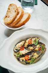 Baked mussels topped with herbs and chilies, served with fresh bread, make a tasty seafood dish