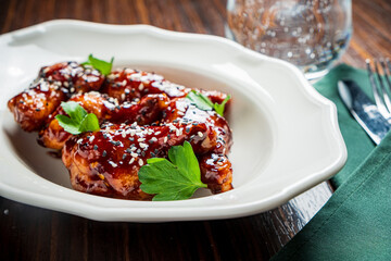 Tasty chicken wings in sweet sauce, topped with herbs, served at a cozy table