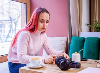 Young woman writing in a notebook studying at a cafe table. Concentrated young woman with bright hair in a cozy cafe setting.