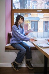 Young woman listening to music on headphones and enjoying a book and coffee in a cozy cafe 