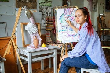 Young female artist draws colorful illustrations in a creative studio. The artist paints a still life with watercolors.