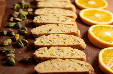 Gourmet, homemade pistachio and orange zest biscotti cookies, arranged with pistachio nuts and orange slices on a wood cutting board