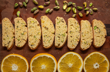 Pistachio and orange biscotti cookies arranged on a wood cutting board with pistachios and orange slices