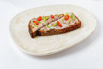 A unique sandwich features a hearty bread base topped with savory spread, herbs, and chili