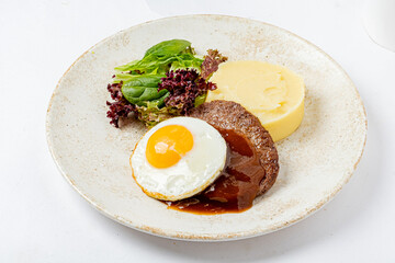 A sunny-side-up egg tops tender beef, served with creamy mashed potatoes and greens