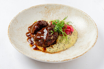 Tender beef in rich sauce on creamy mashed potatoes, topped with herbs and pickles