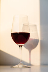 Fototapeta premium A beautifully filled glass of red wine stands tall, surrounded by gentle light and shadows
