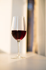 A single glass of rich red wine sits on a simple table, glowing in soft afternoon light